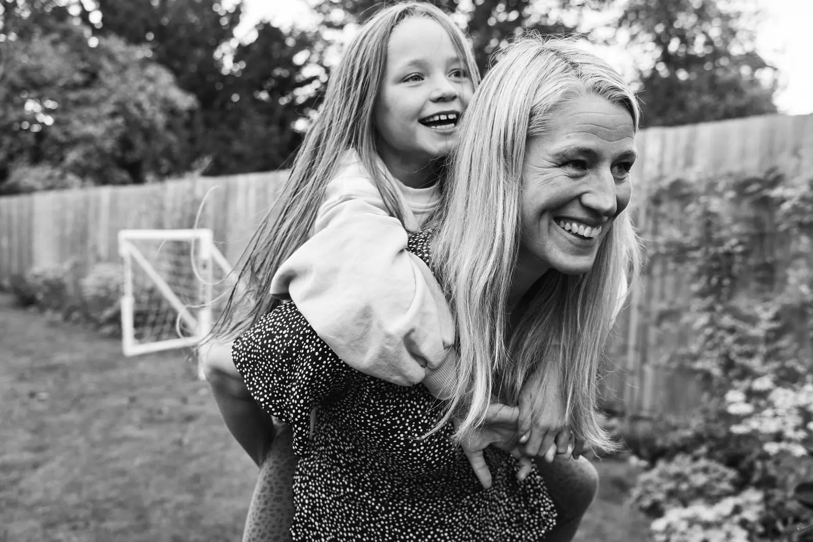 Mother carrying her daughter on her back laughing together — fun documentary family photography Bromley