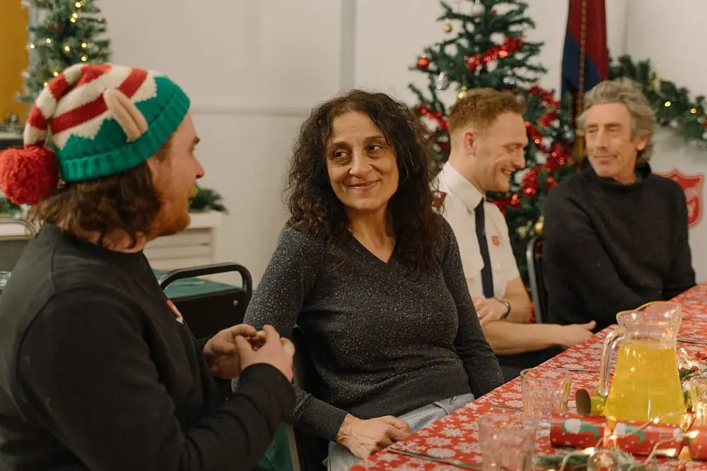 Models and Salvation Army staff chatting and smiling around a festive table at a community Christmas lunch.