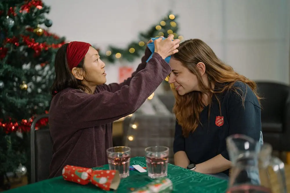 Woman placing a paper Christmas crown on a Salvation Army staff member’s head at a community Christmas lunch. Models used.