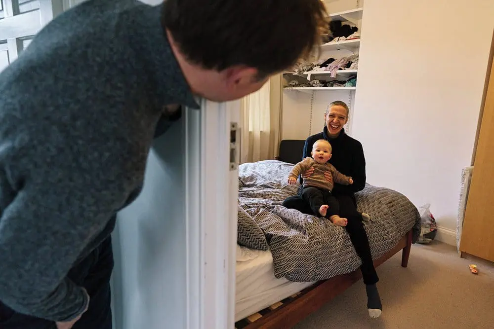 Father playing peekaboo with his baby around the door — joyful candid family photography South-East London