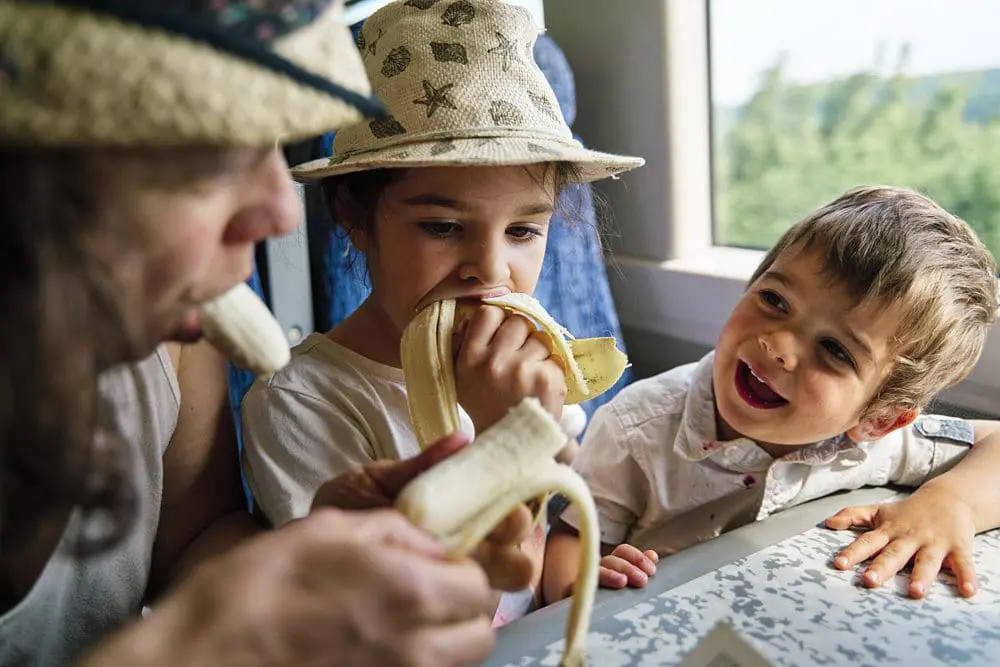 Family laughing and eating bananas on a train outing — reportage family photographer London