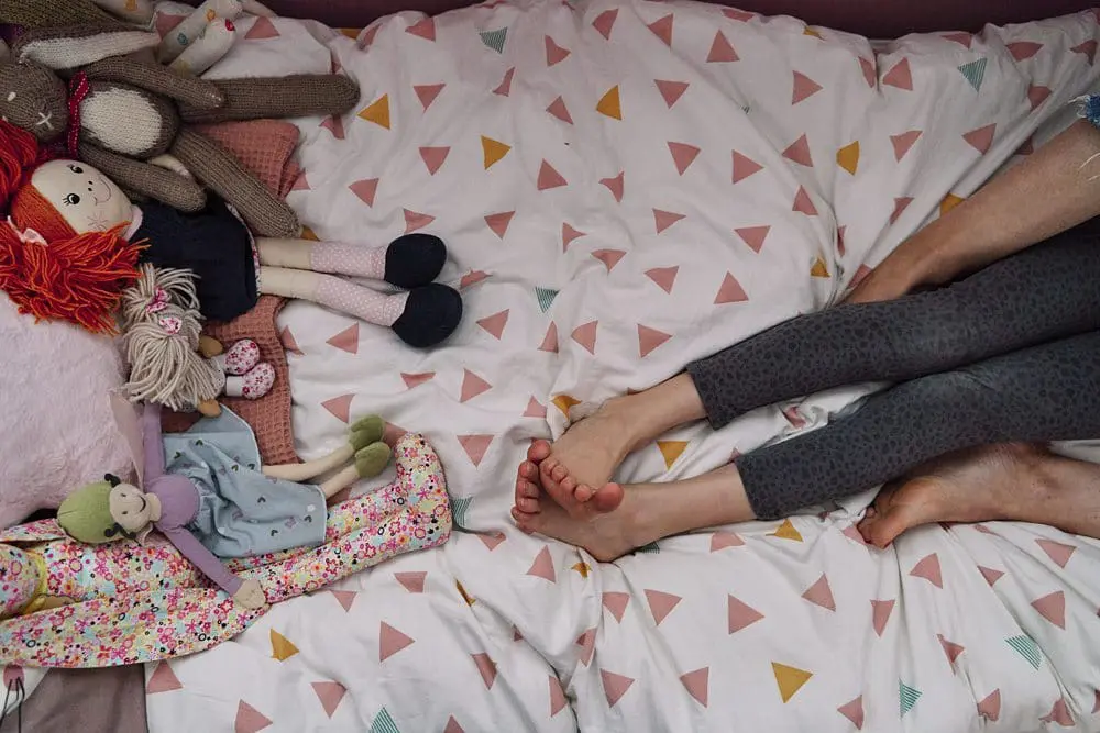 Peer reviewed playful documentary image of mum and daughter's legs opposite a row of stuffed toy legs