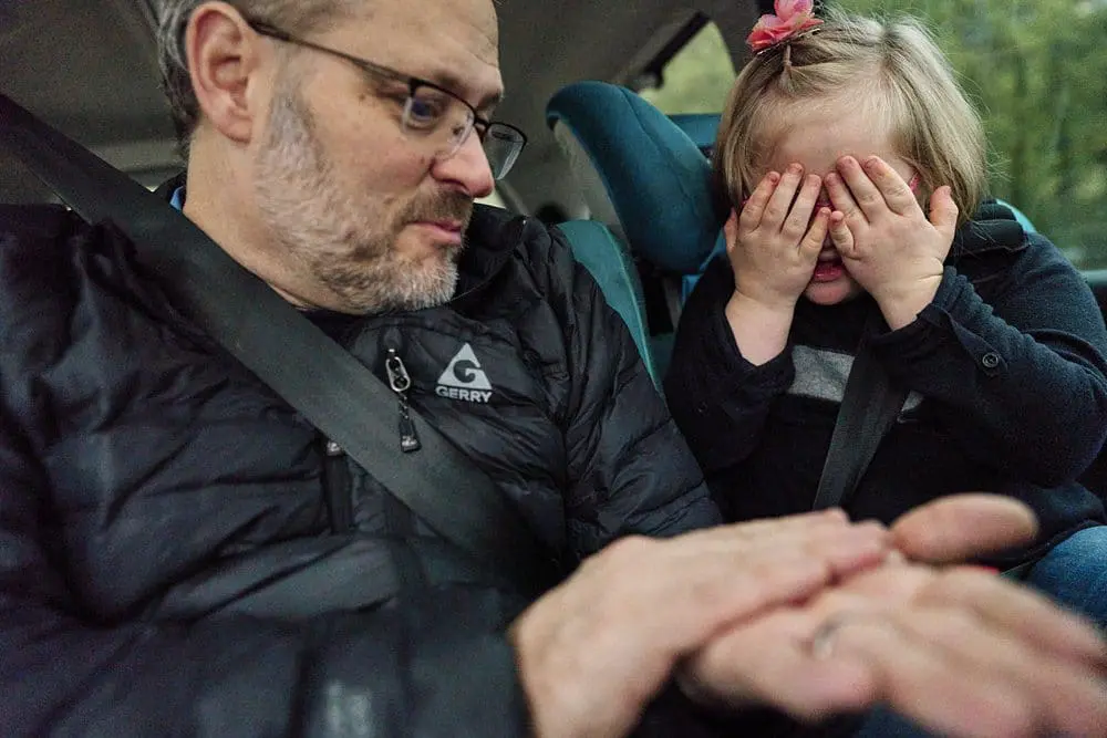 Father and daughter playing a hiding coin game in the car, daughter covering her eyes laughing — candid family photographer South-East London