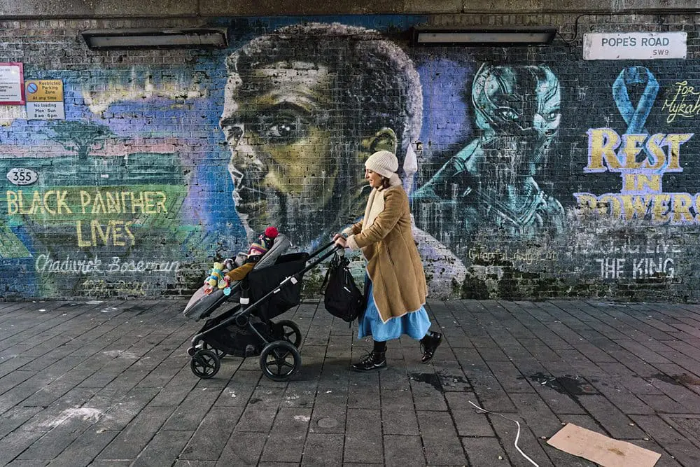 Mother pushing pram in front of London street art — documentary family photographer London