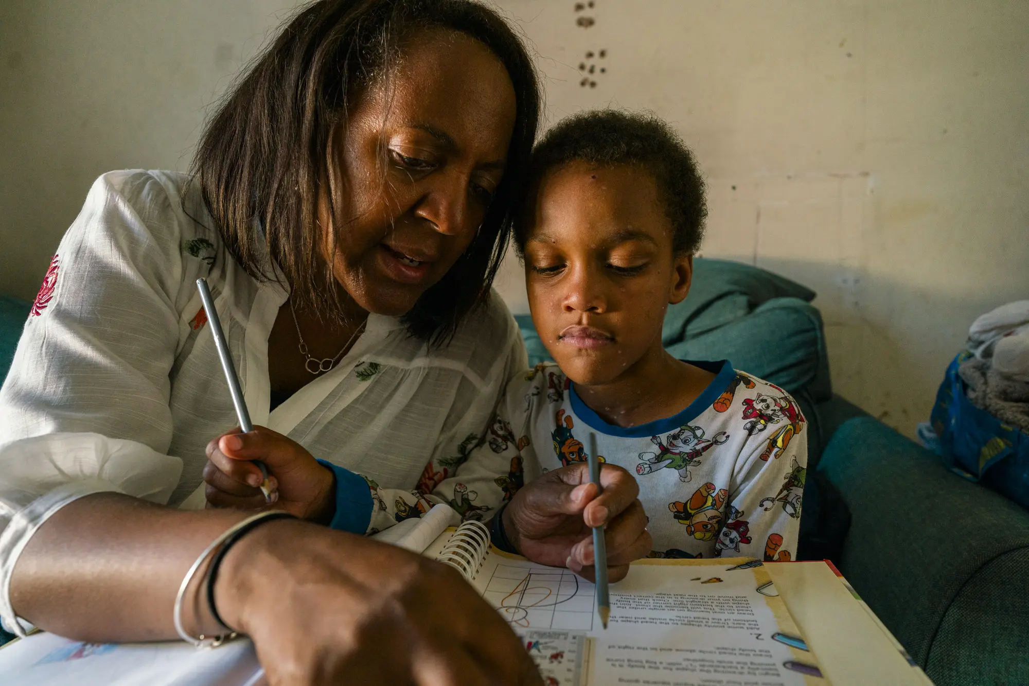 Kinship carer helping her young grandson with his homework at home, documentary charity photography for Kinship