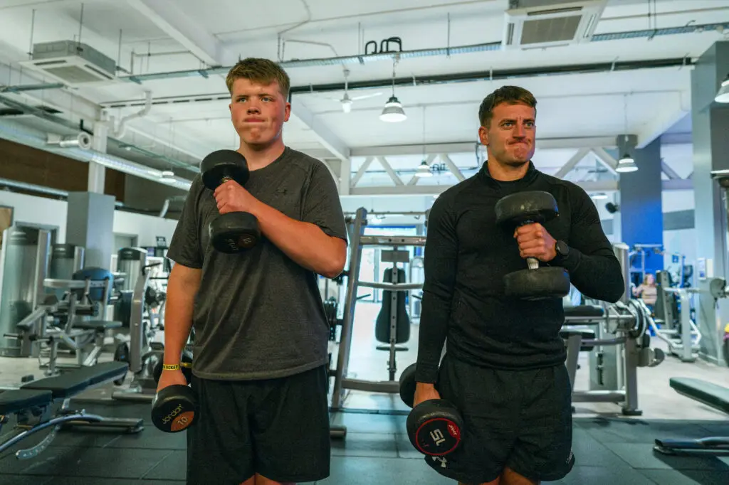 Kinship carer and his teenage brother lifting weights together at the gym, an authentic moment no AI image could capture.