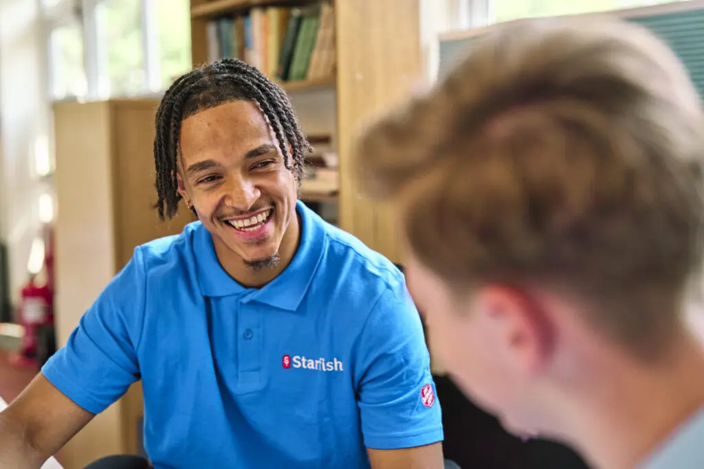 Smiling Salvation Army Starfish youth worker in a charity polo shirt chatting with a young person — candid charity photography UK