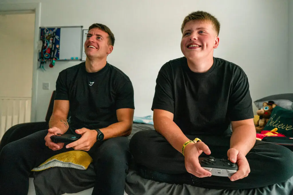 Kinship carer and his teenage brother laughing together as they play a video game — charity documentary photography UK