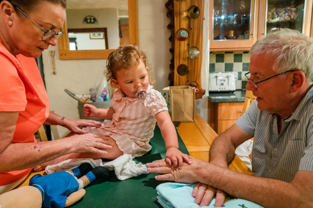 Grandparents and kinship carers getting their toddler granddaughter ready for bed at the kitchen table — honest documentary photography for Kinship