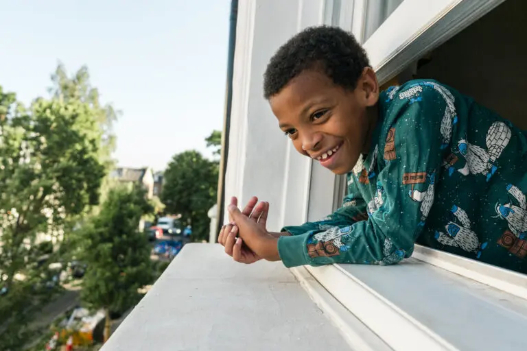 Smiling boy leaning out of his open window at home in London, from a documentary photo series about kinship families.