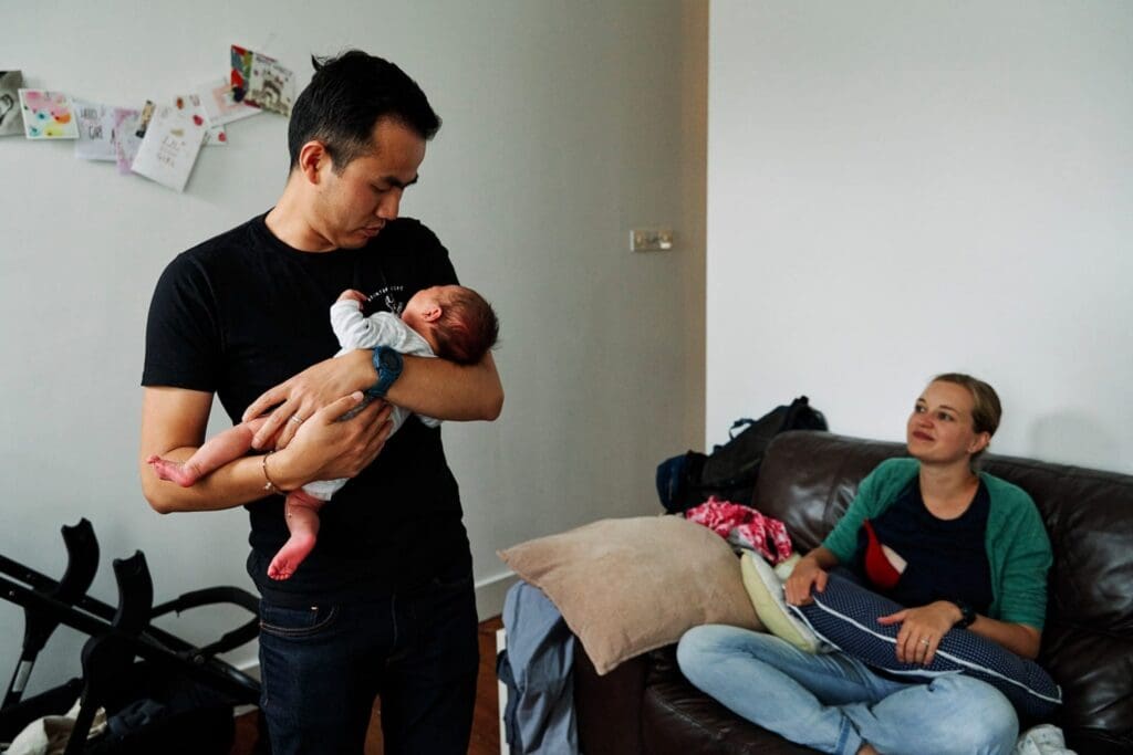 Father holding newborn to give to mother for a feed during a newborn photography shoot.