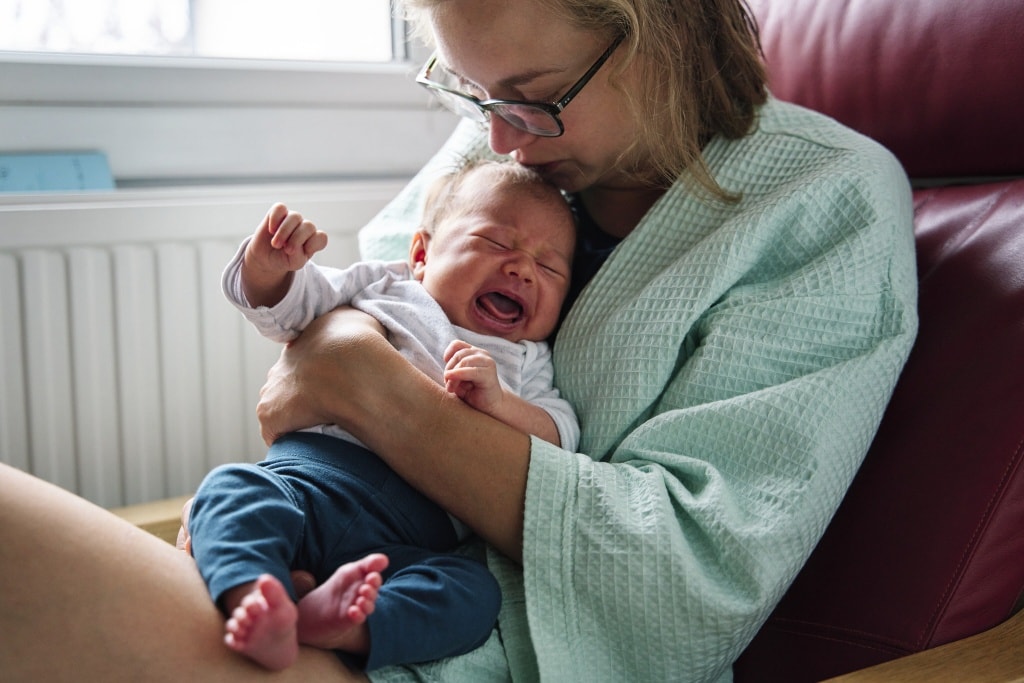 Photograph of a crying newborn being comforted in mothers' arms during a newborn photography session in Bromley.