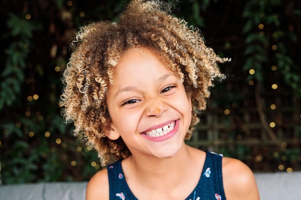 Photograph of girl smiling at the camera with some tomato sauce on nose during a family photography session in Bromley South-East London