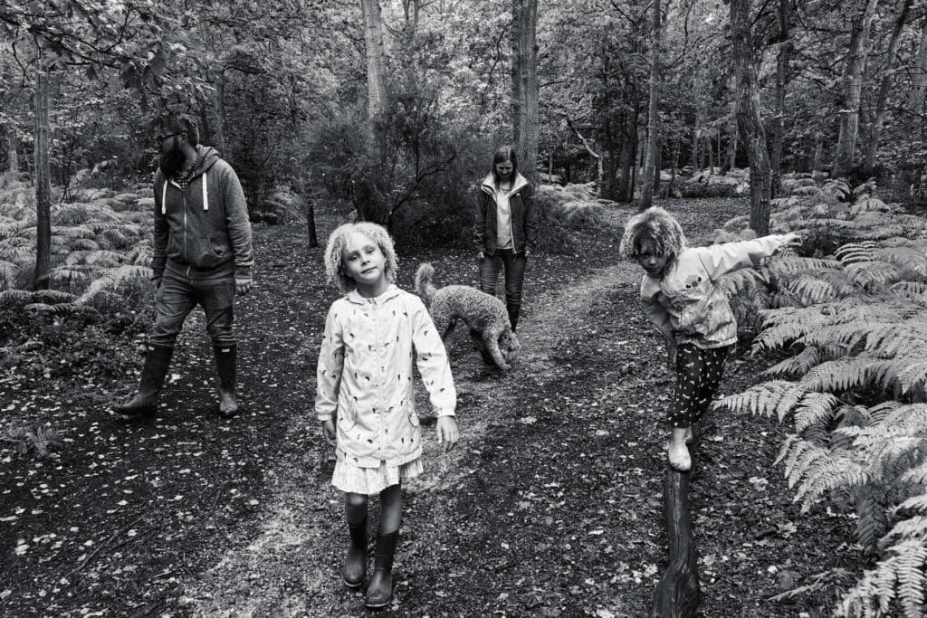 Black and white documentary style photograph of family walking in the woods of Hayes Common in Bromley during a family photography session
