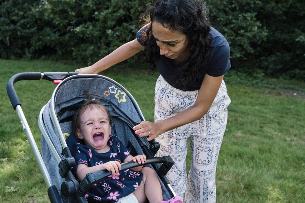 Authentic family portrait of a child crying in the pram while parent tries to console her. 