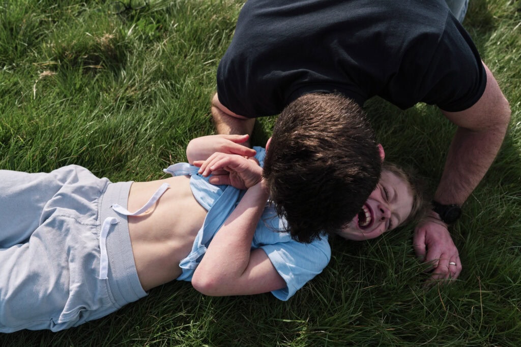 Dad and child playing rough in a park during a documentary family photo session for reluctant dads