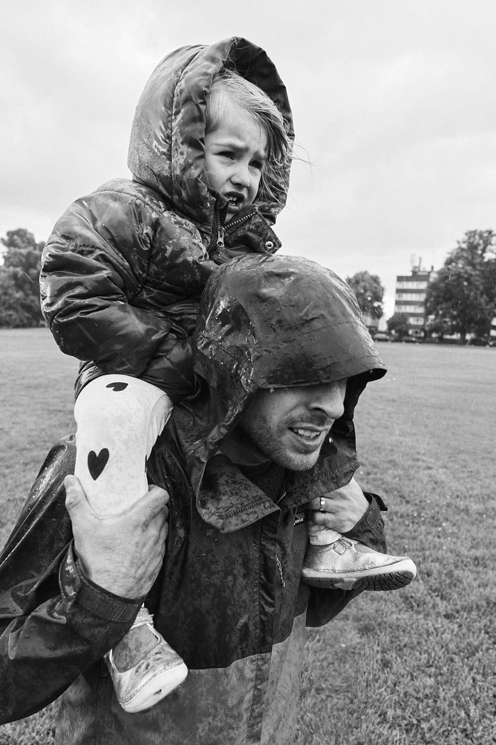 Father carrying daughter on his shoulders walking through rain in Dulwich Park — candid family photographer Dulwich