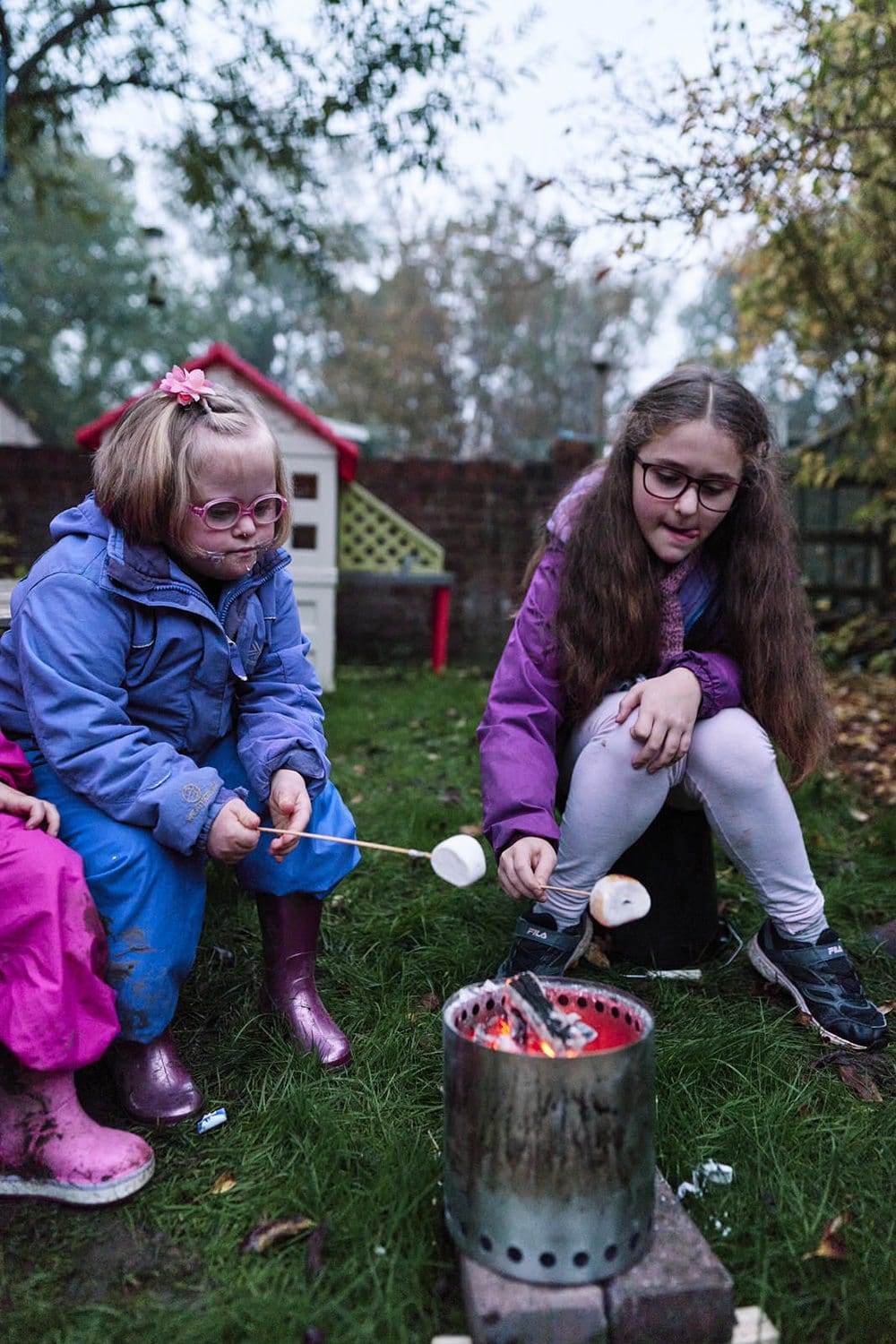 Two sisters roasting marshmallows together in the garden — fun candid family photography Greenwich