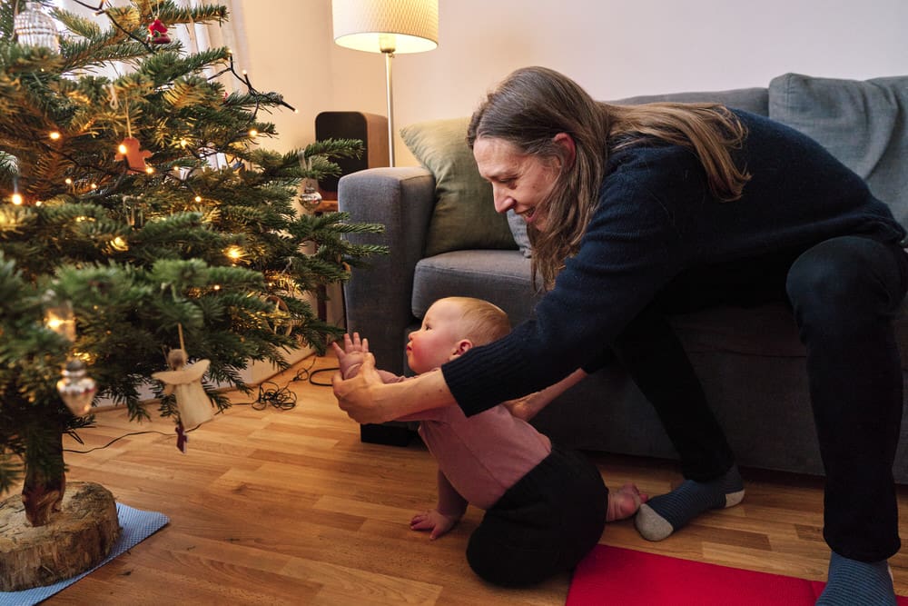 Baby reaching out to touch the Christmas tree as mum holds her hand — intimate Christmas family photography Crystal Palace