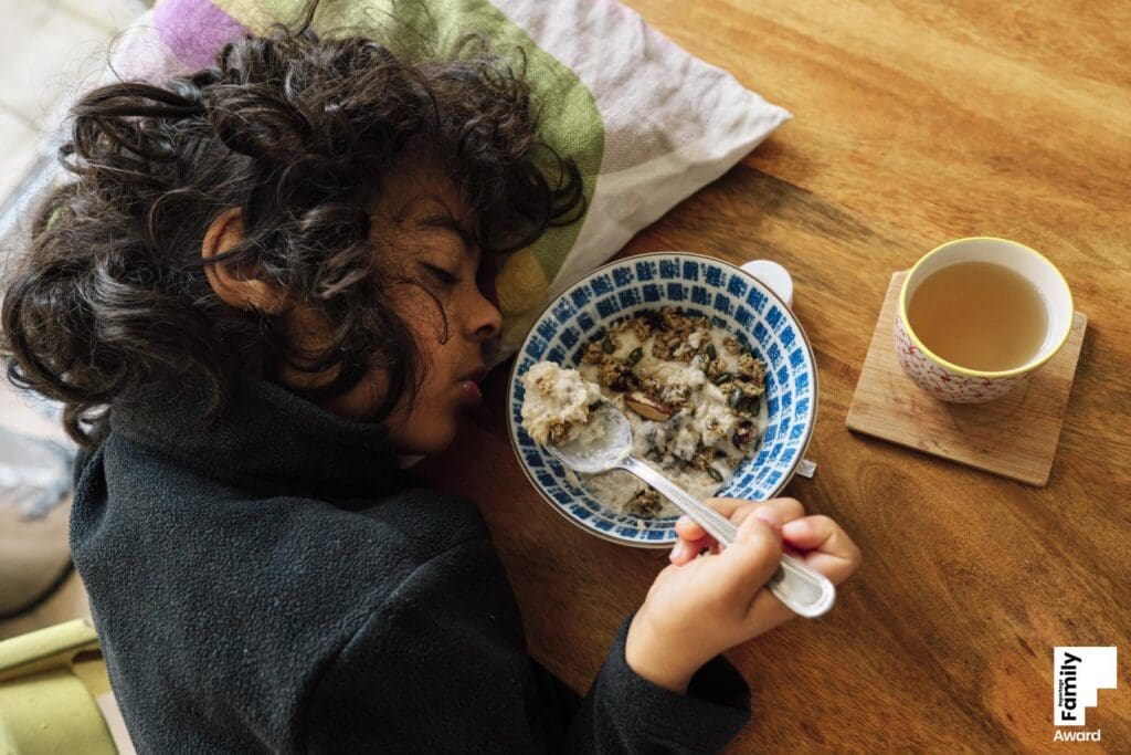 An award-winning family photograph of a child sleeping while eating his breakfast in London UK