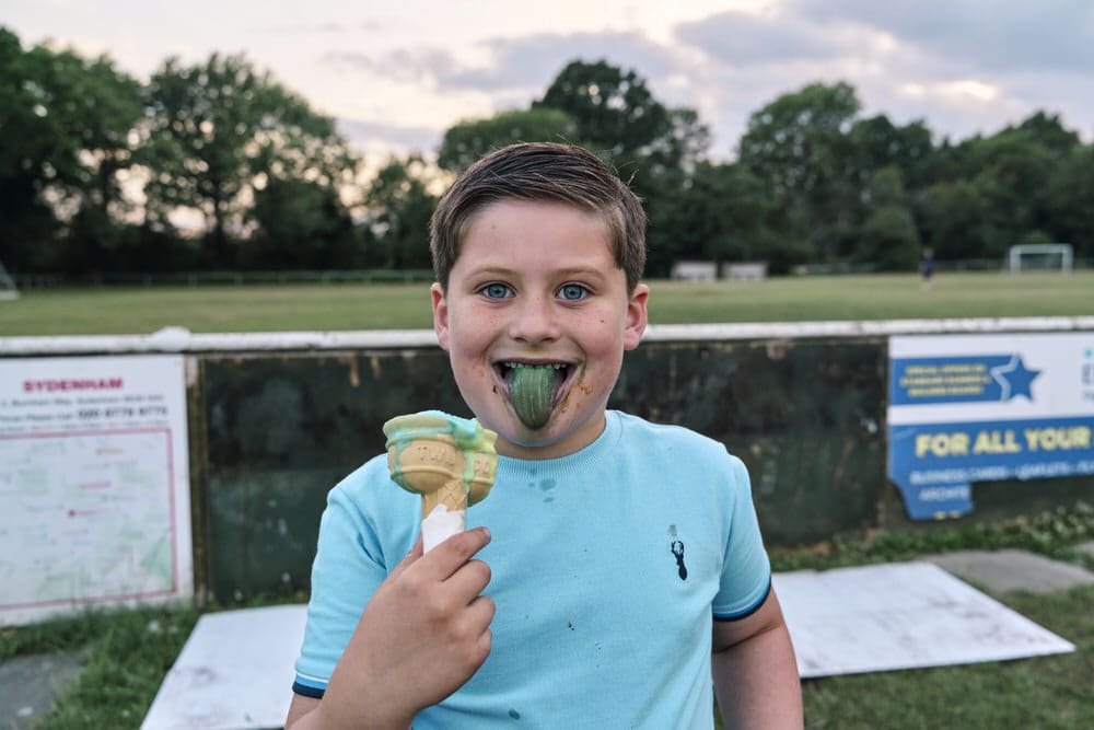 London documentary family event photographer capturing boy sticking out coloured toung from eating an ice cream at a family party.
