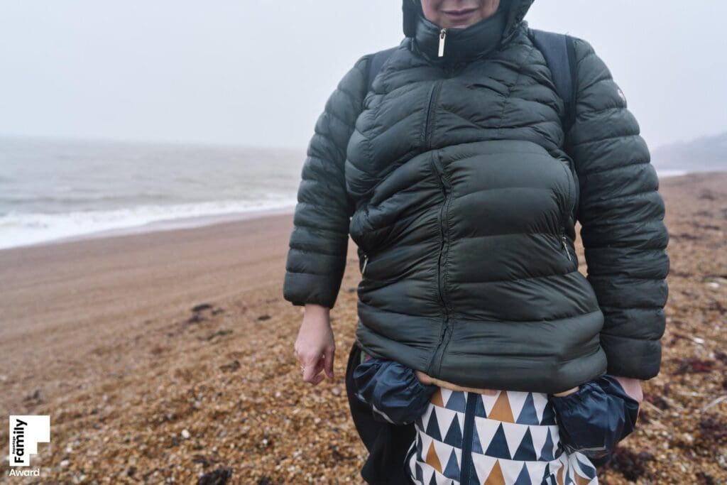 Documentary family photographer London working with family during a natural photography session taking a picture of an autistic son hiding under his mothers coat.
