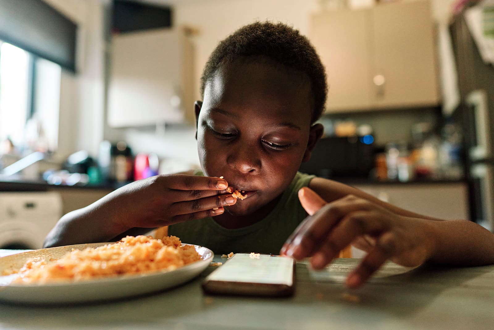 Autistic child eating while watching a mobile phone during a neurodivergent-friendly documentary family photography session in London.