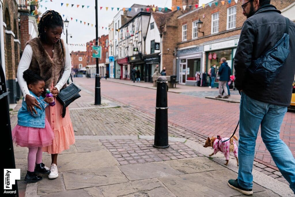 Natural real-life family photograph of child scared of a dog walking by hiding behind her mother in London taken by a Top 10 UK documentary family photographer